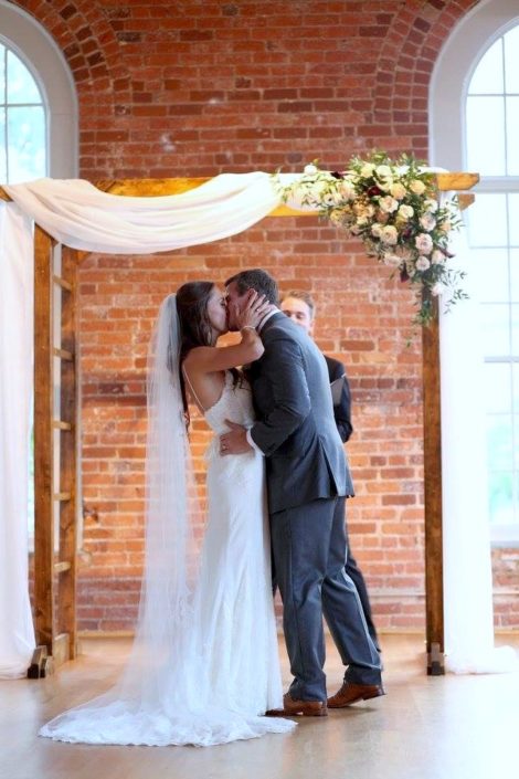 bride and groom kiss under ceremony arbor flowers