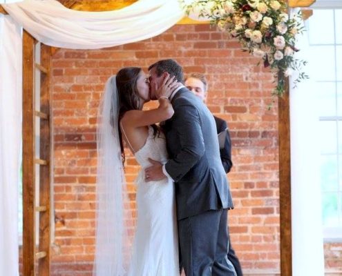 bride and groom kiss under ceremony arbor flowers