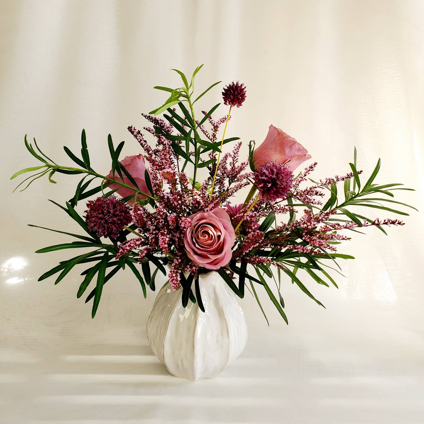 Array of blooms with pink roses and greenery in a white vase designed by durham florist poppy belle floral design