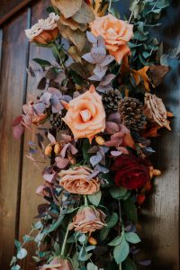 Fall display of blooms with accent of pinecones creating a beautiful hanging impressive display for family gatherings on holidays of oranges, red, and pinecones designed by durham florist poppy belle floral design