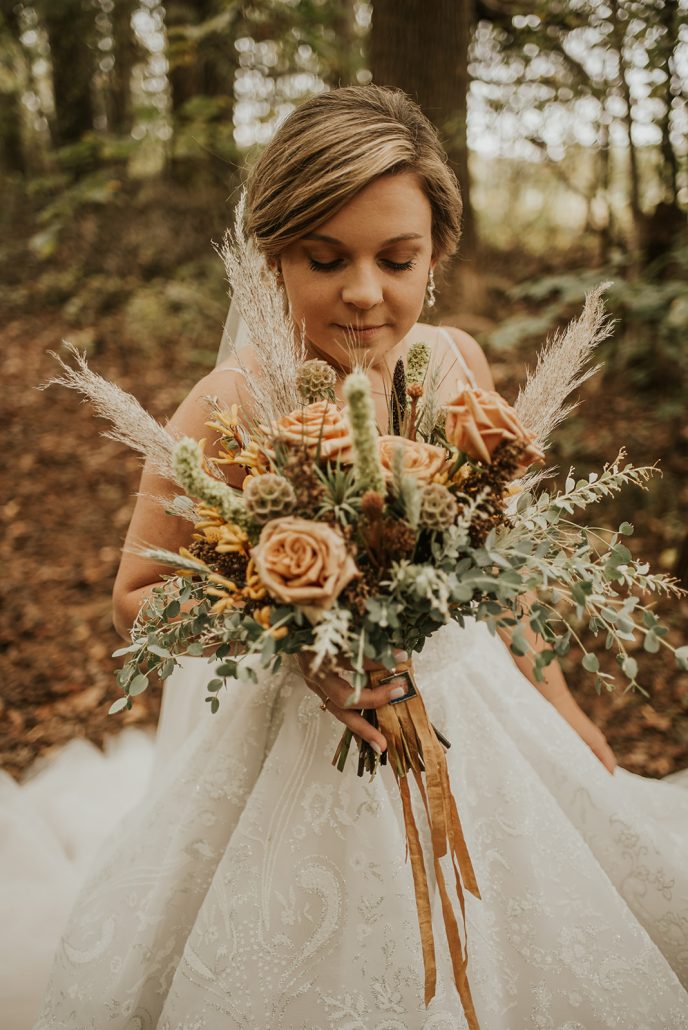 Bride in woods holding Bridal bouquet with greens dusty coral and texture for boho wedding designed by durham florist poppy belle floral design
