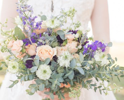 Purple, coral and white blooms with greenery pulled together in a beautiful bridal bouquet designed by durham florist poppy belle floral design