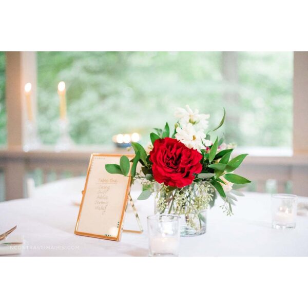 Centerpiece with red and white blooms and greenery next to sign designed by durham florist poppy belle floral design