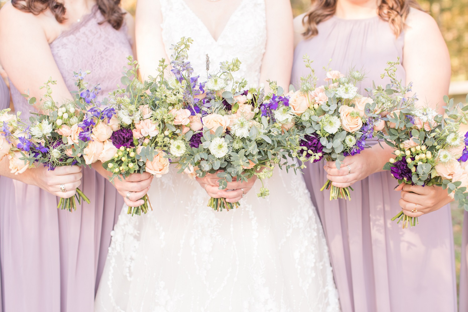 Bride in v neck white wedding dress holding Purple, coral and white blooms with greenery pulled together in a beautiful bridal bouquet designed by durham florist poppy belle floral design